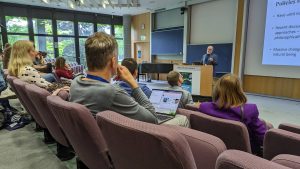 Man stands at lectern in front of group of seated scientists