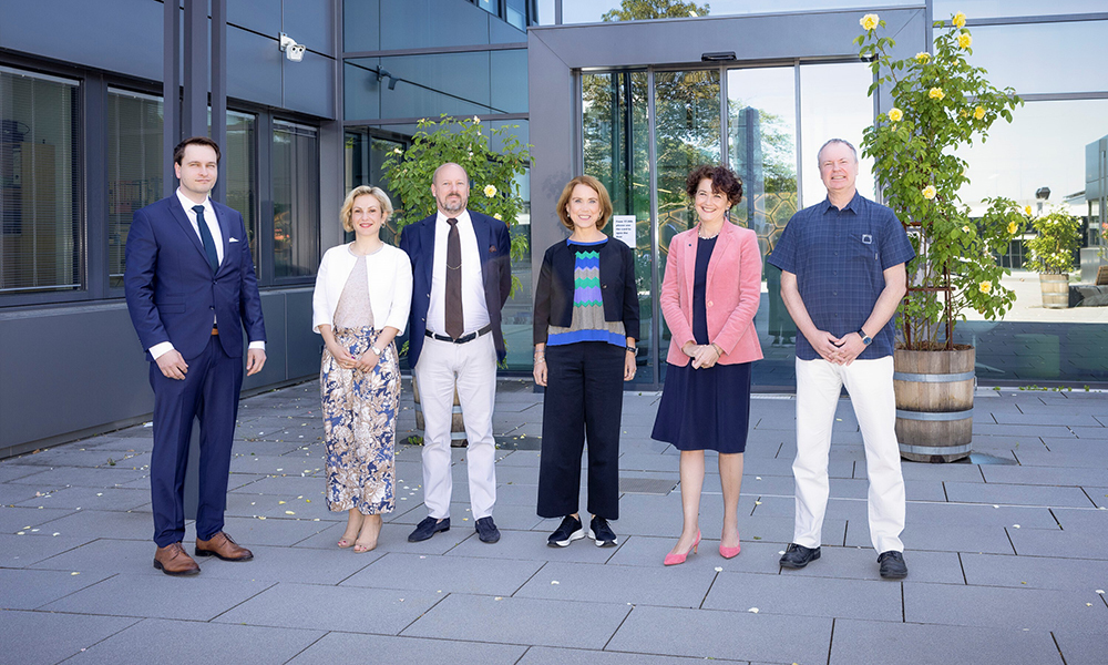 Minister Petra Olschowski and members of EMBL staff and directorate are standing in front of the EMBL Heidelberg main entrance.