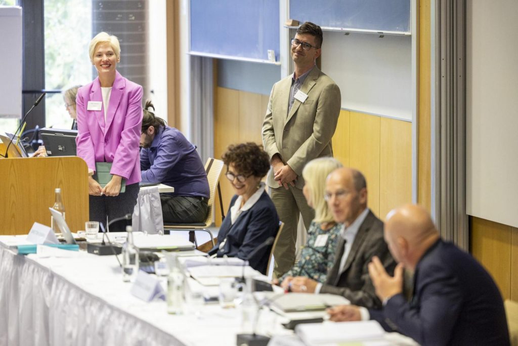 Council members at front of meeting room converse with one another.