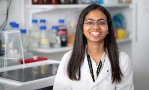 Woman wearing lab coat in laboratory environment. It is a portrait of Rutuja Yelmar, Indian woman with long dark hair.