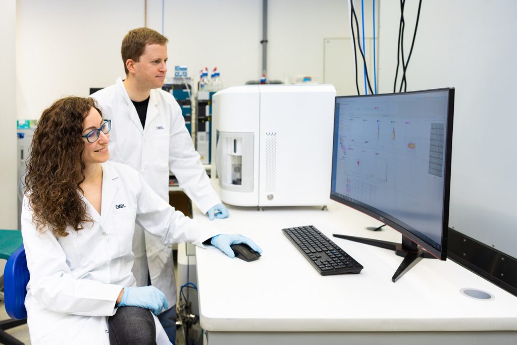 Two scientists wearing lab coats look at a screen that shows the results of an ICS sorting experiment. 