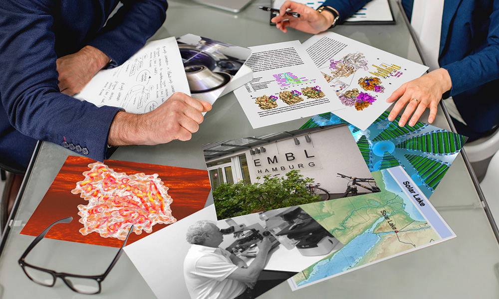 Photo of two people brainstorming at the table covered with several papers and images related to the research project, such as the structure of the molecule, a map with the Solar Lake marked, photo of EMBL Hamburg, photo of Garo Antranikian looking into a microscope, pages of the manuscript, data graphs, and more.