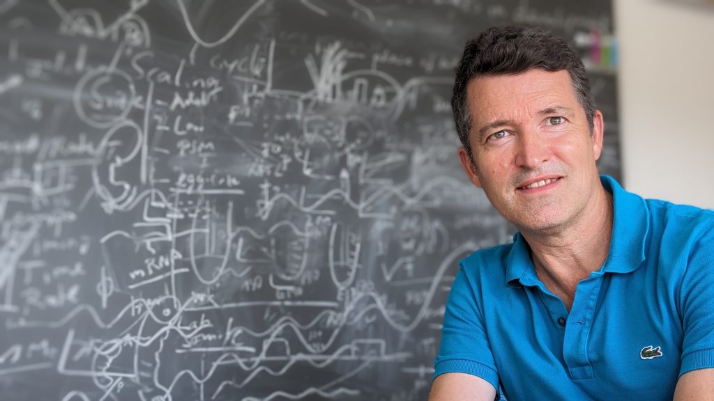 A male scientist in front of a chalkboard.