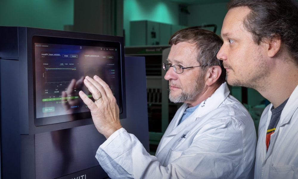 Two male scientists in lab coats looking at.a computer screen