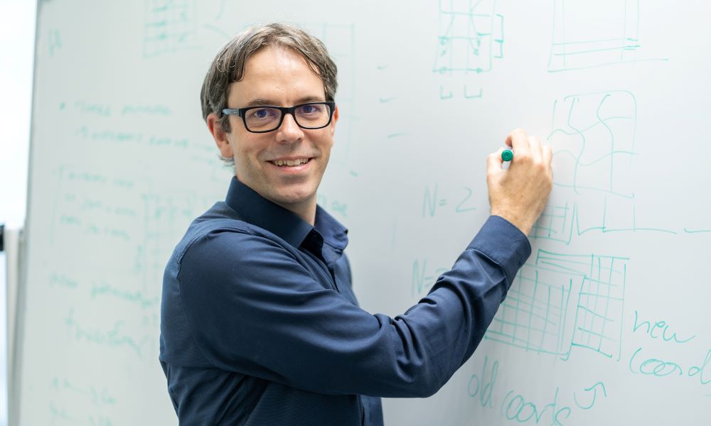 Oliver Stegle passionately drawing work-related content with a green pen on a whiteboard. On the whiteboard, there are coordinates and equations, such as “n=2”.