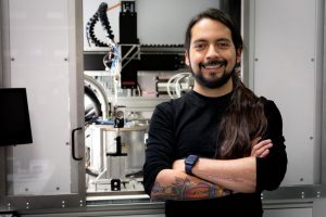 Man in long-sleeved black shirt stands in front of machinery