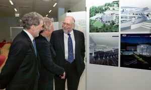 Two men and a woman are discussing the new ATC in front of building plans shared at the groundbreaking ceremony.