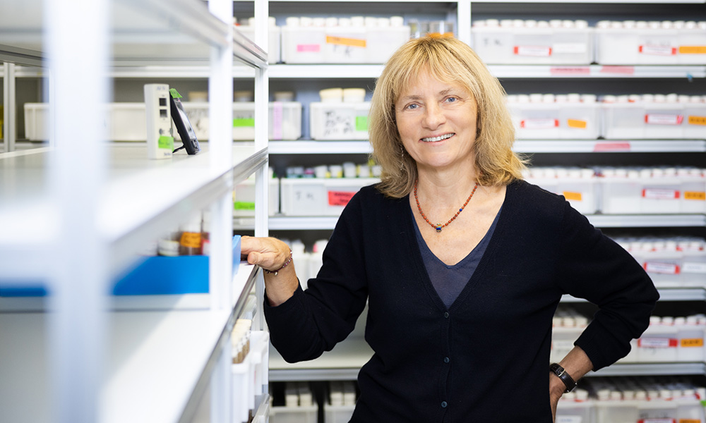 Female scientist stands in front of white shelves filled with vials of fruit flies