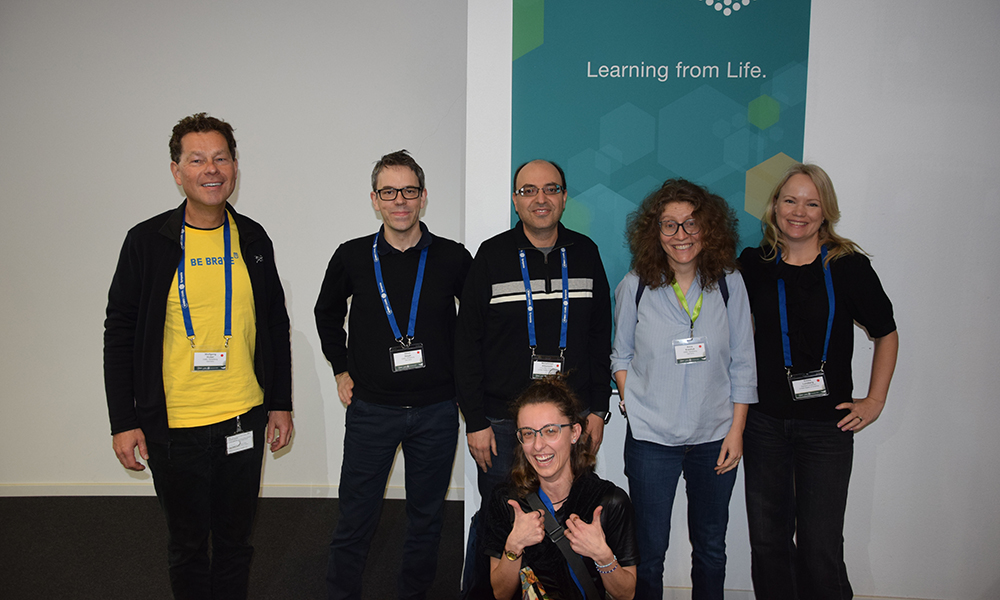 Six scientists at a conference in front of a banner.