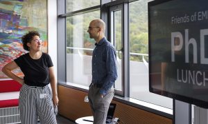 Two scientists stand in front of window, talking