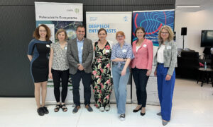 Seven people standing in front of three posters at an event.