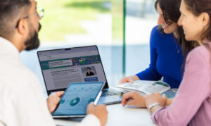 Three people huddled around a laptop and tablet.