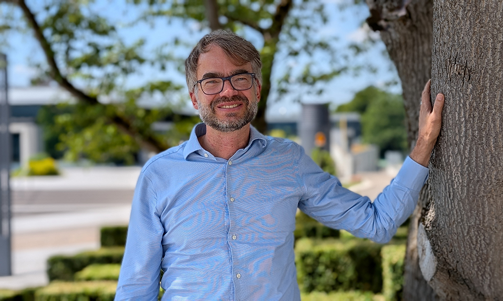 Male scientist in blue shirt standing next to a tree outdoors.