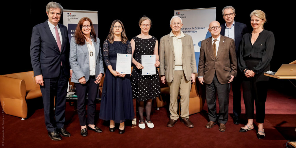 From left to right: François Delattre (Ambassade de France), Christina Gommlich (BASF), laureates Stefanie Kaiser (Goethe-Universität Frankfurt) and Eva Kowalinski (EMBL Grenoble) -holding their respective awards, Jean-Marie Lehn (1987 chemistry nobel prize winner and eponymous patron of the prize), Antoine Triller (Académie des Sciences), Christian Lerche (Sanofi), and Eva Martha Eckkrammer (UFA) standing on stage during rhe Forcheurs Prize ceremony in Berlin.
