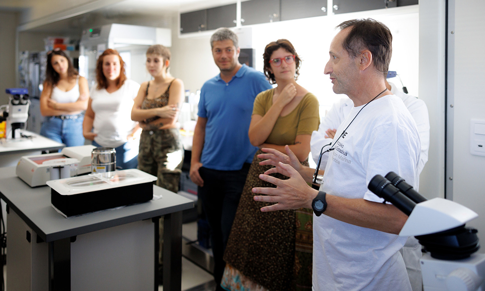 A scientist explaining something to a group of observers inside a laboratory.