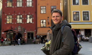A man is smiling. Colourful houses of Gamla Stan are visible in the background.