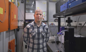 A man is standing next to a bench in a room with experimental equipment.