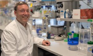 Male scientist sits at lab bench, staring ahead