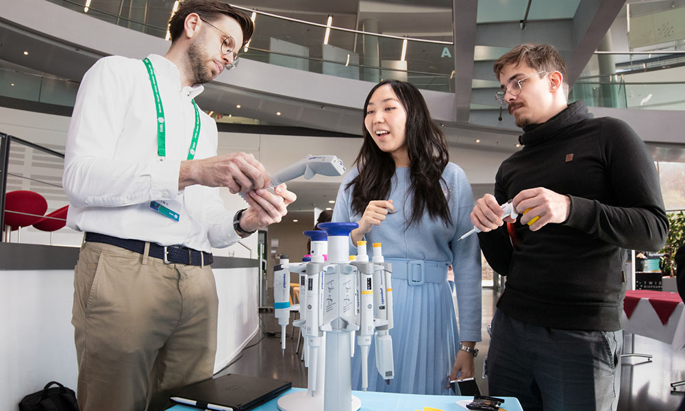 Company representative shows a digital pipette to two scientists.