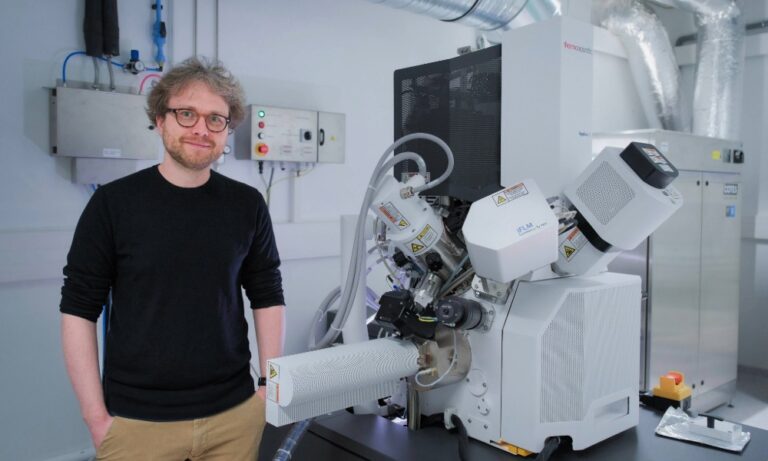 Florian standing next to a large microscope in a laboratory setting, smiling at the camera
