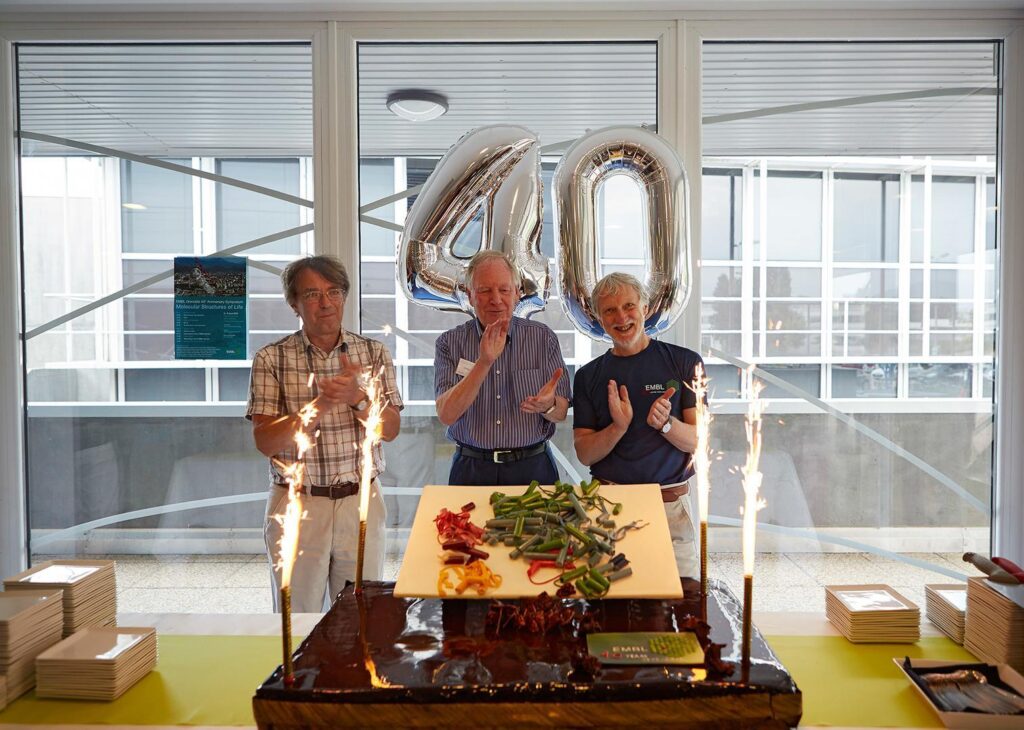 Stephen Cusack celebrates the 40th anniversary of EMBL Grenoble in 2015, with Andrew Miller, the first Head of EMBL Grenoble (1975-1980), and Iain Mattaj, EMBL Director General (2005-2018), with a chocolate incarnation of the influenza polymerase in front.
