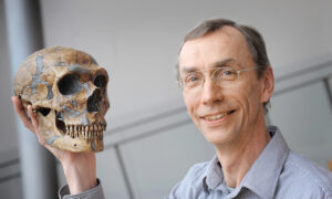 Scientist holding a Neanderthal skull and looking at the camera.